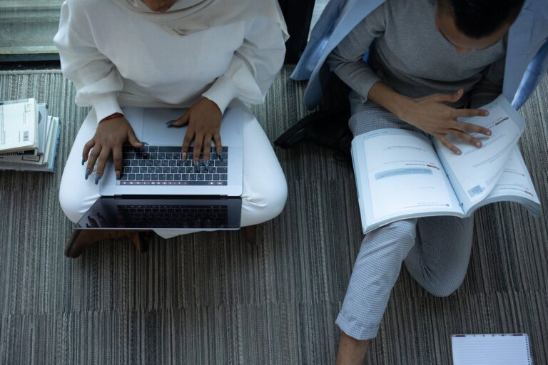 Two students of colour. One reads on computer one reads a print textbook.