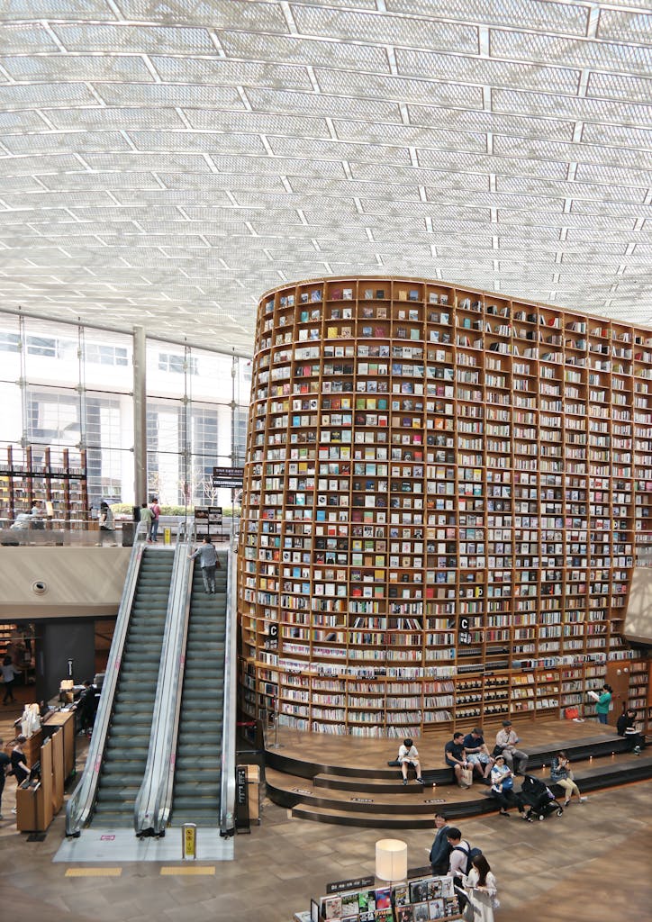 Books In a Library on an architecturally interesting but impossibly tall bookshelf that requires an escalator to access