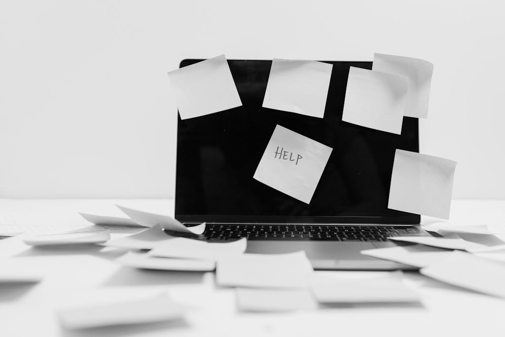 Sticky Notes on a Laptop and all over a desk. One posted in the middle of the laptop screen reads help.