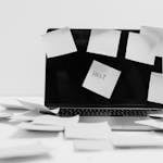 Sticky Notes on a Laptop and all over a desk. One posted in the middle of the laptop screen reads help.