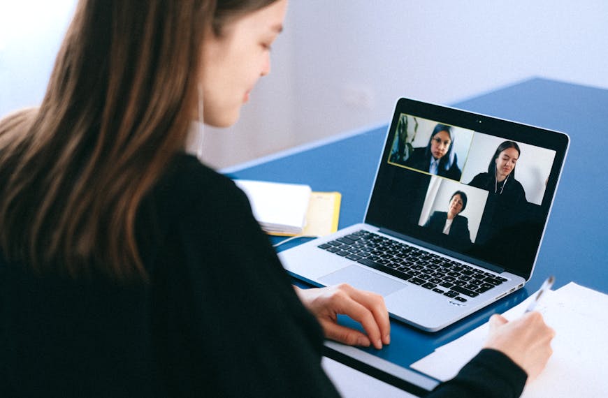 A woman engaging in a video conference using a laptop at home, taking notes.